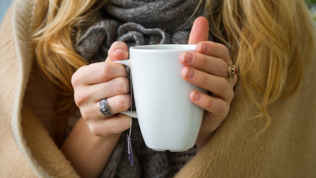 Eine Frau mit Schal und Decke hält eine Teetasse in Händen