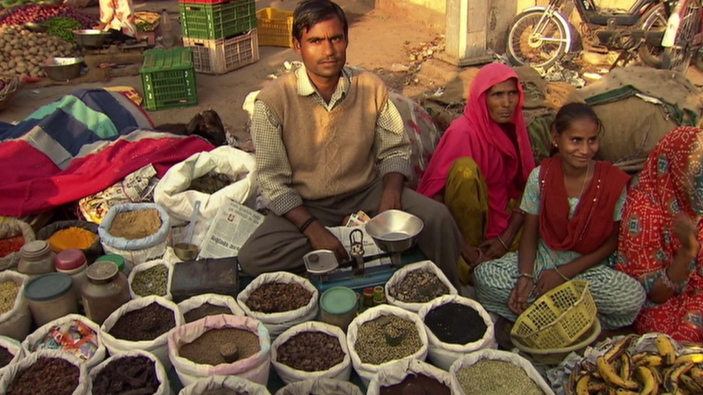 Foto: Ein Mann, eine Frau und ein Mädchen sitzen vor Körbern voller Gewürzen an einer indischen Straße.